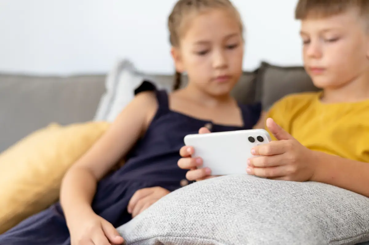 Two children sitting together indoors, focused on a smartphone screen, symbolizing digital habits and the importance of balance and mindfulness in technology use.