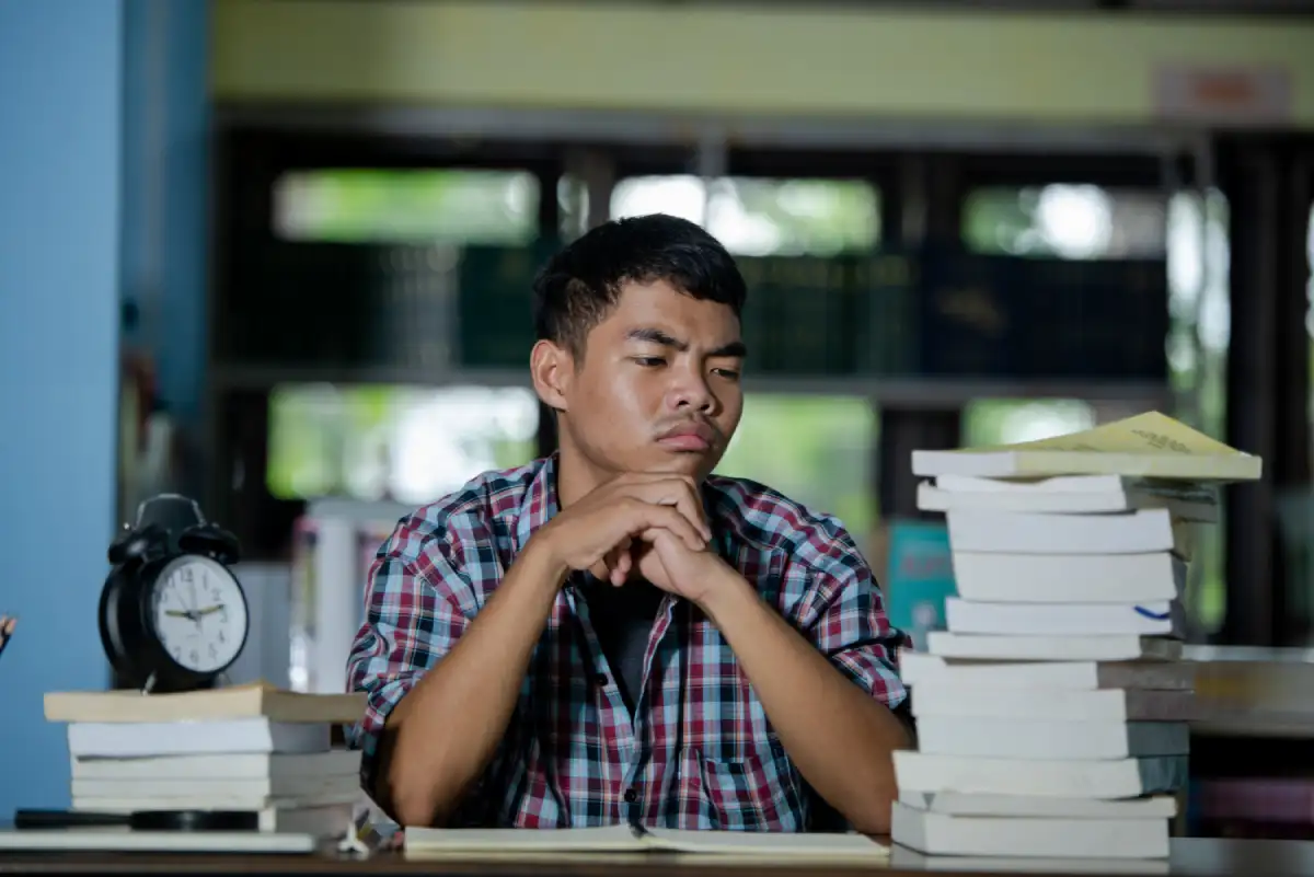 Tired Indian student studying in a library and feeling exam stress, representing the need for emotional support and stress management in schools.