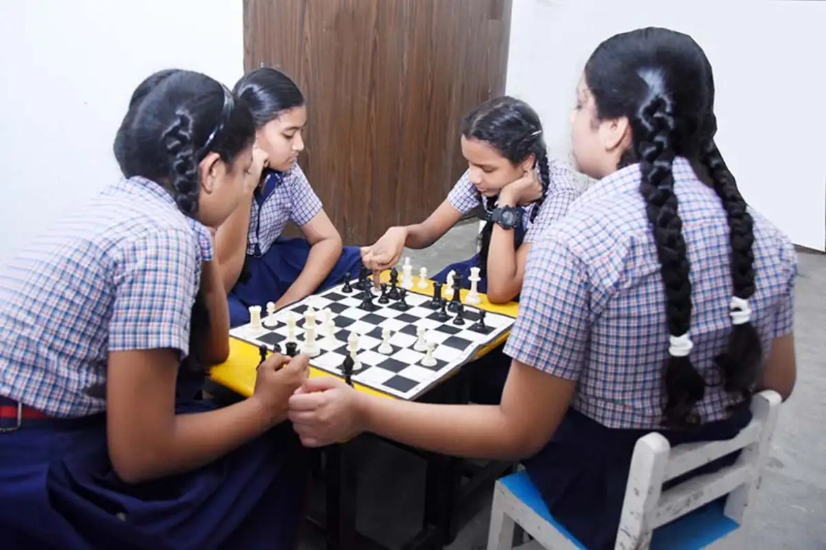 School girls in uniforms playing chess together at a table in a classroom